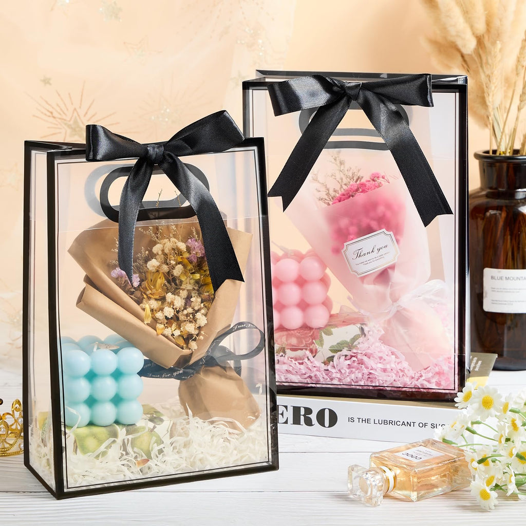 Two clear plastic gift bags with black ribbon handles, each containing decorative items like dried flowers and candles.