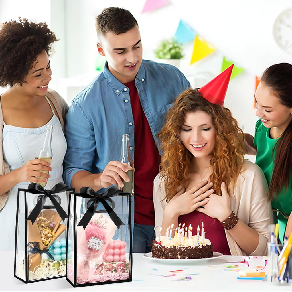 Two clear plastic gift bags with black ribbon handles, filled with decorative items, sit on a table next to a birthday cake and people celebrating.