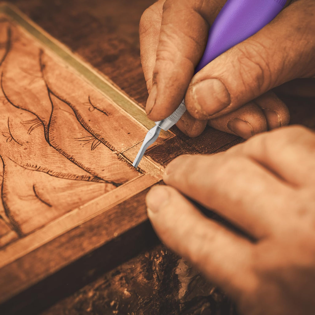 Close-up of hands using a linoleum cutter tool with a purple handle to carve a design into wood.