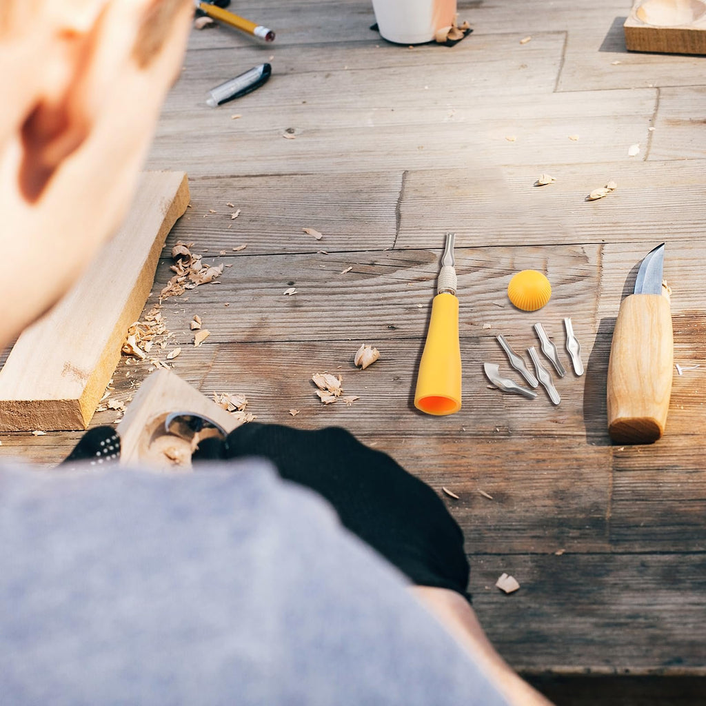 Close-up overhead view of a person carving wood with a linoleum cutter kit on a wooden table.