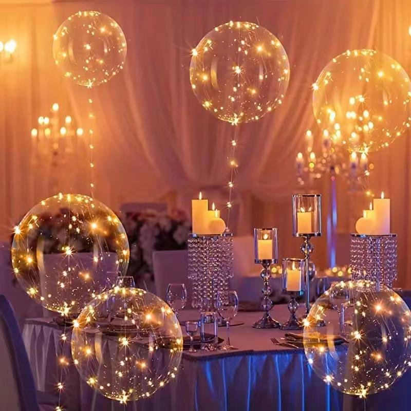 Clear LED light-up balloons with warm white string lights floating above a decorated table setting with candles.