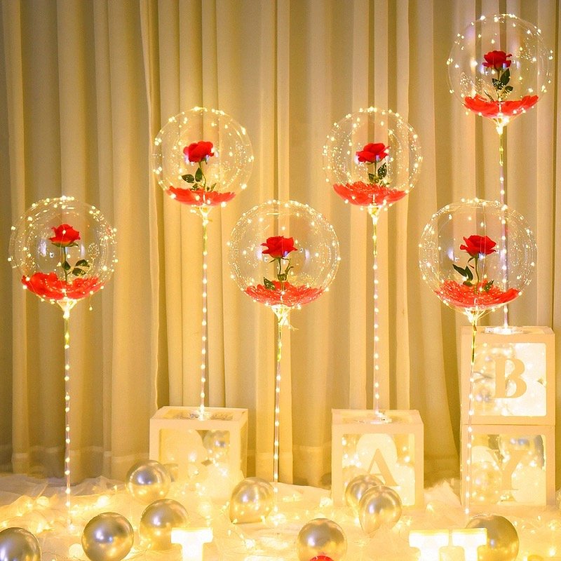 Six clear LED light-up balloons with red roses and warm white string lights, arranged with decorative boxes and balloons.