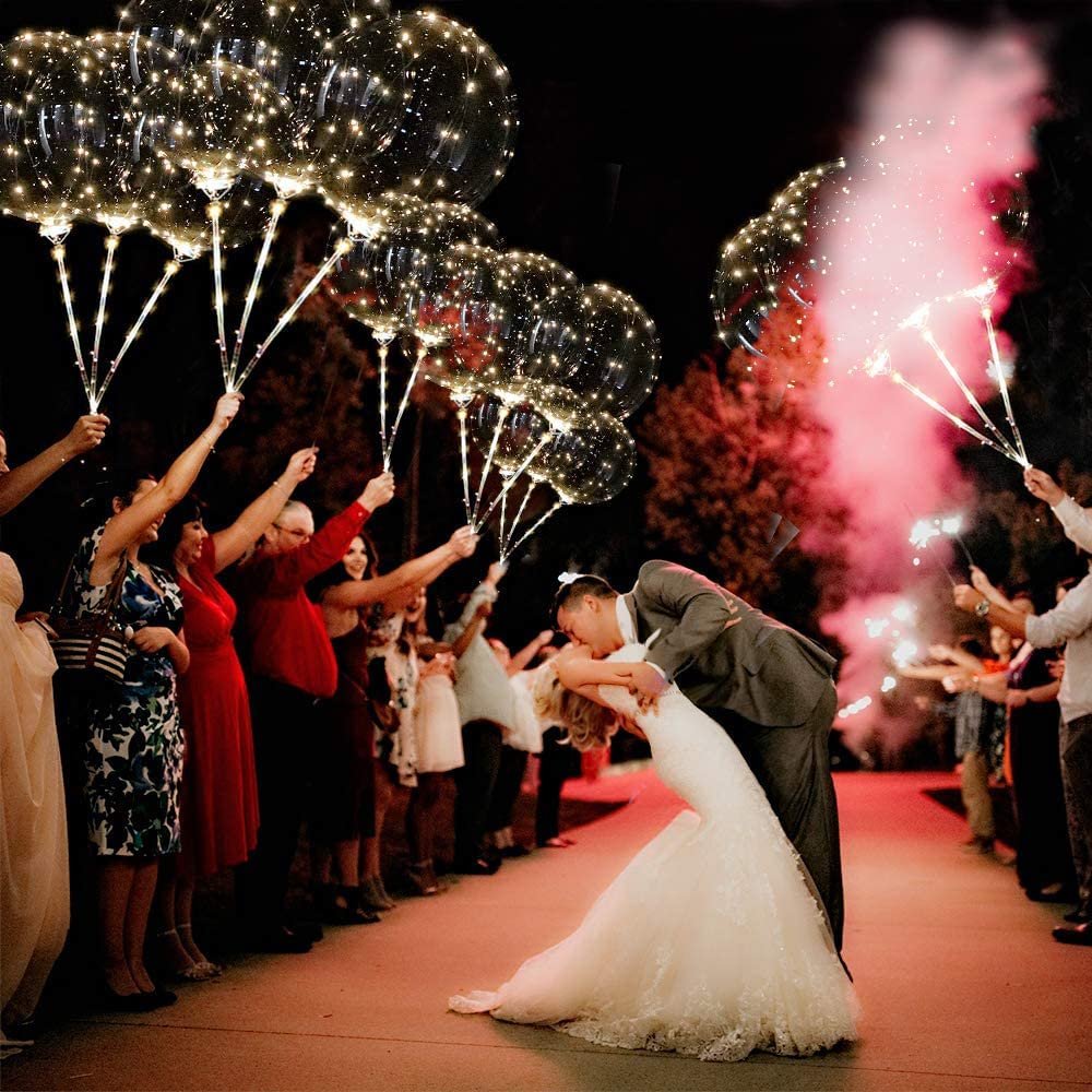 Wedding couple kissing surrounded by guests holding LED light-up balloons and sparklers