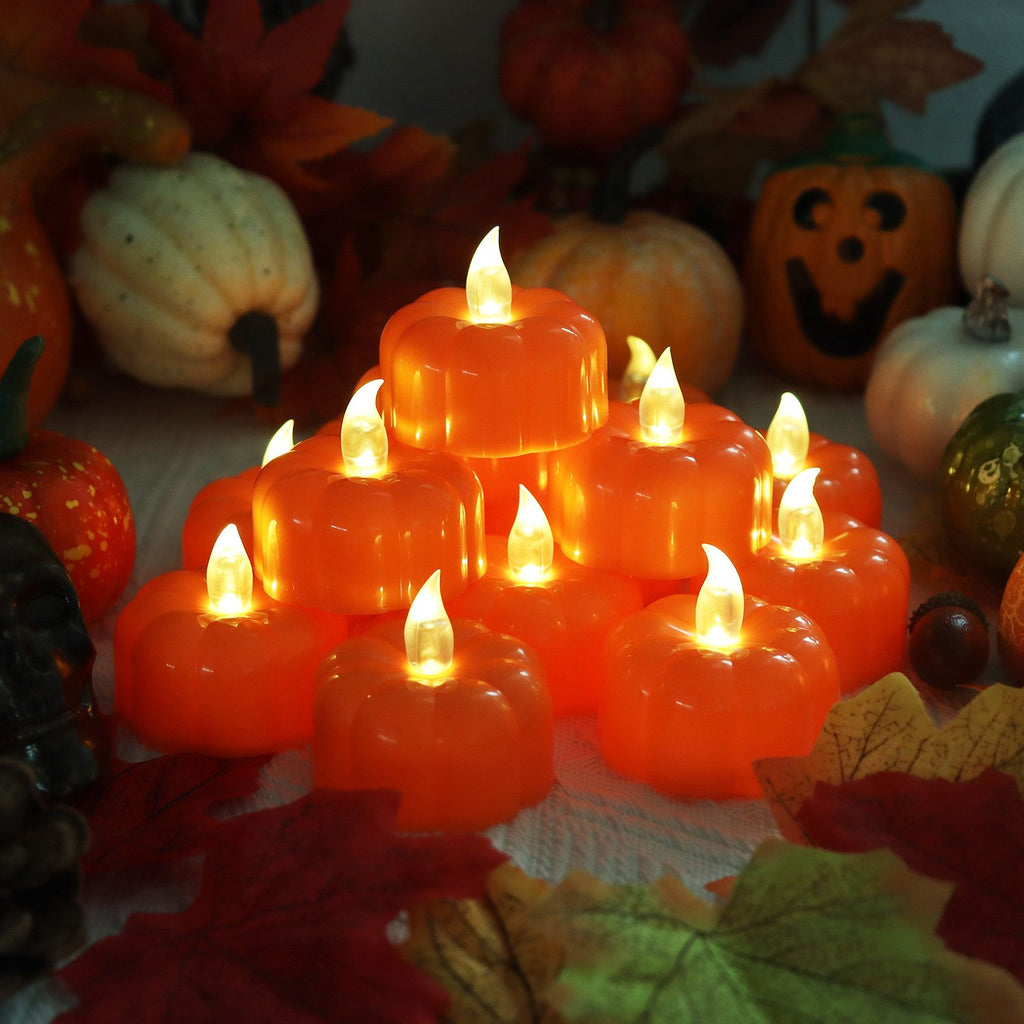 Pile of orange LED pumpkin tea lights with flickering flames, surrounded by decorative pumpkins and autumn leaves.