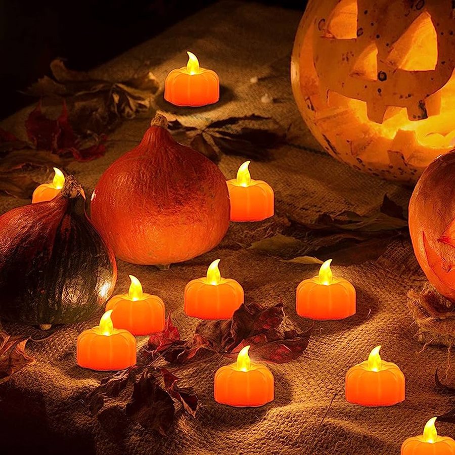 Group of orange LED pumpkin tea lights scattered on burlap with real pumpkins and a carved jack-o'-lantern