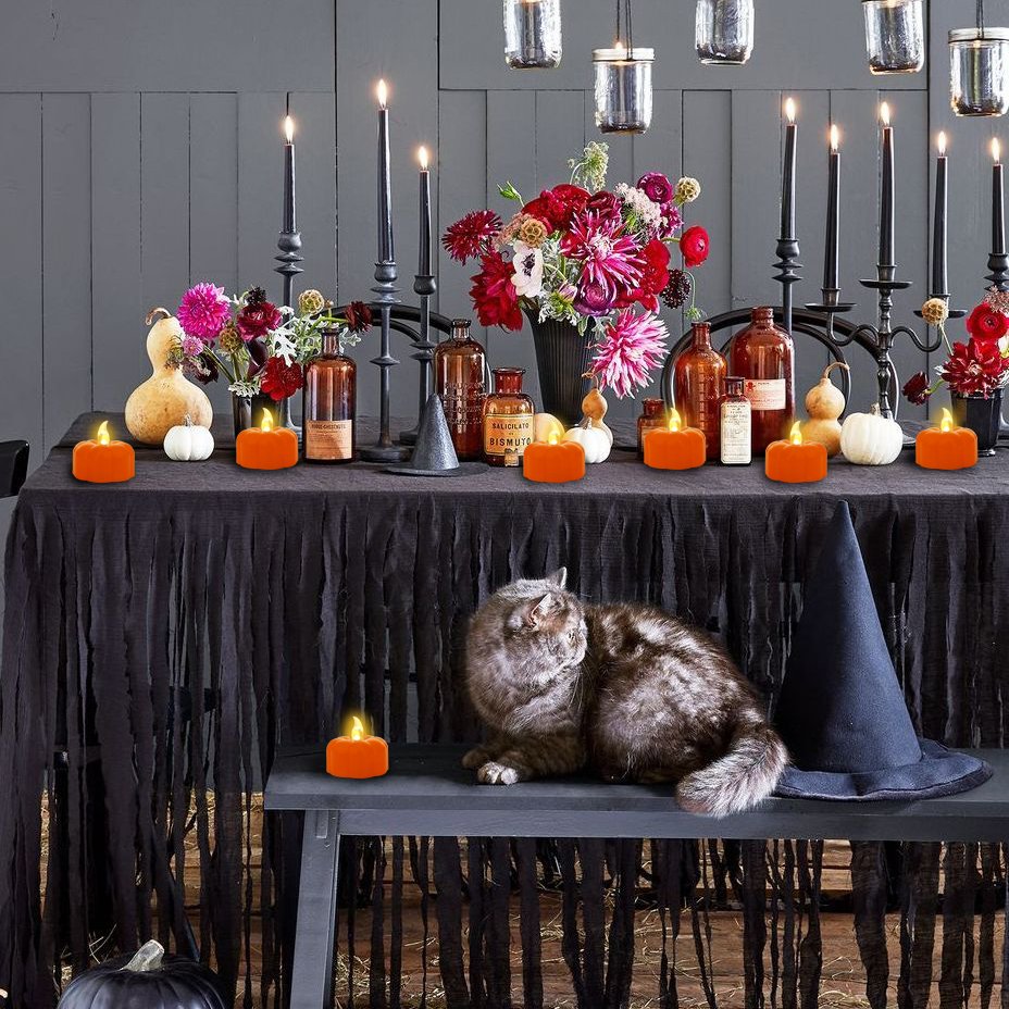 Halloween table setting with orange pumpkin tea lights, flowers, and a cat on a bench.