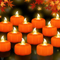A dozen orange LED pumpkin tea lights with flickering flames arranged in rows on a dark reflective surface, with autumn leaves at the top.