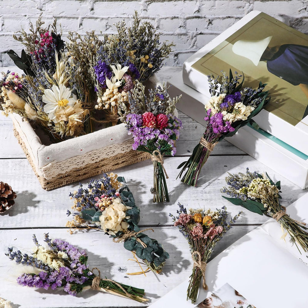Assortment of mini boho dried flower bouquets arranged on a white wooden surface with a basket and books.