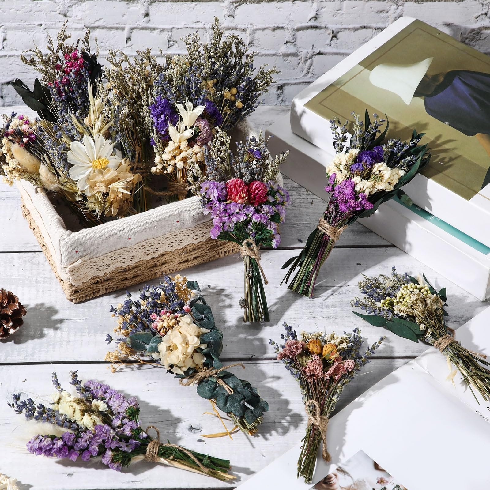 Assortment of mini boho dried flower bouquets arranged on a white wooden surface with a basket and books.