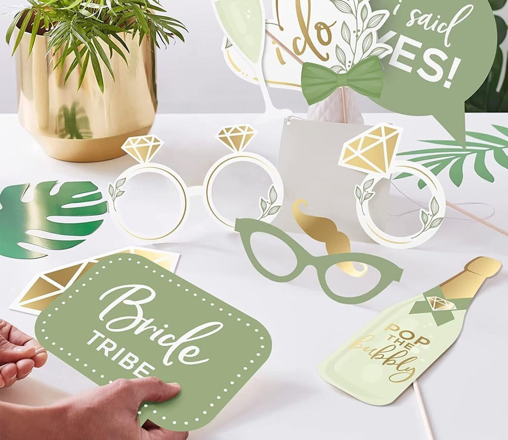 Wedding photo booth props kit with rings, glasses, bow tie, and speech bubbles on a white table.