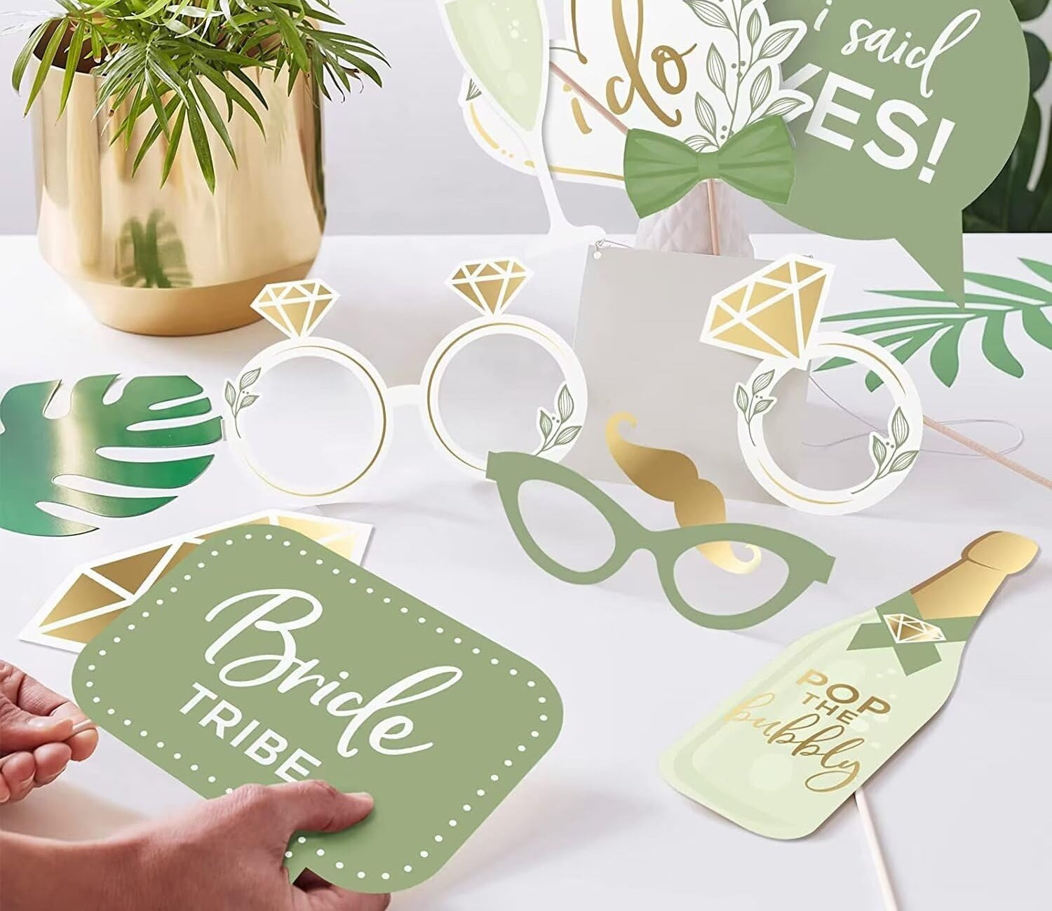 Wedding photo booth props kit with rings, glasses, bow tie, and speech bubbles on a white table.