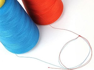 Two large cones of blue and orange polyester serger thread with red and blue threads unspooling on a white background.