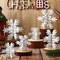 White 3D wooden snowflakes of various sizes displayed on wood slices and logs, with a wooden 'CHRISTMAS' sign above.