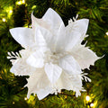 White glitter poinsettia flower with clips and stems on a Christmas tree with lights