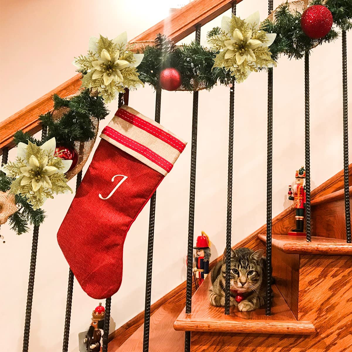 Christmas garland with glitter poinsettias and red ornaments on a staircase railing, with a stocking and a cat.