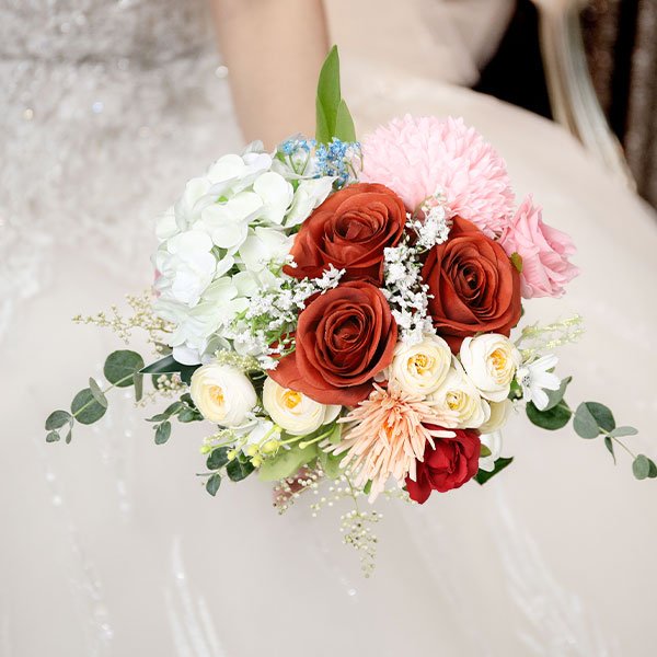 Bride holding a bouquet of artificial burnt orange roses, white hydrangeas, and pink flowers.