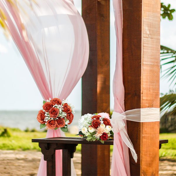 Two bouquets of artificial burnt orange roses and white flowers arranged on a wooden table at a beach wedding ceremony.