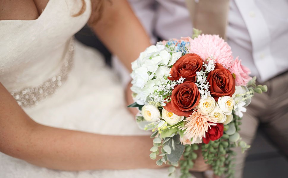 Bride holding a bouquet of burnt orange roses, white hydrangeas, and pink flowers.