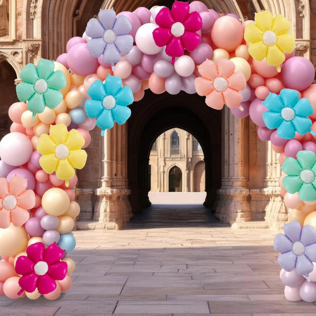 Balloon arch with daisy-shaped foil balloons in pastel colors, set against an arched stone building entrance.