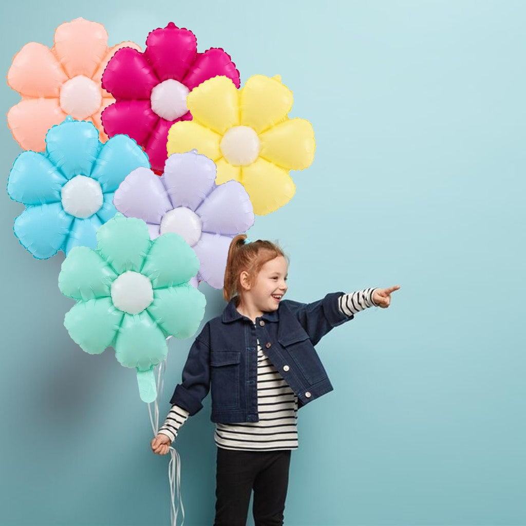 Girl holding a bunch of colorful daisy-shaped foil balloons and pointing to the right against a light blue background.