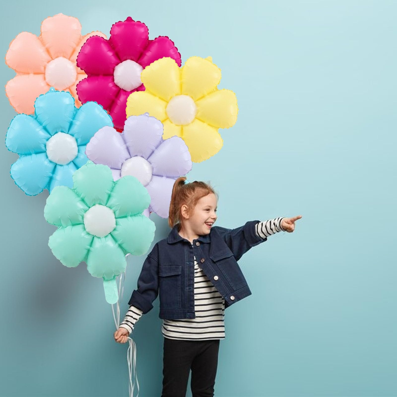 Girl holding a bunch of colorful daisy-shaped foil balloons and pointing to the right against a light blue background.