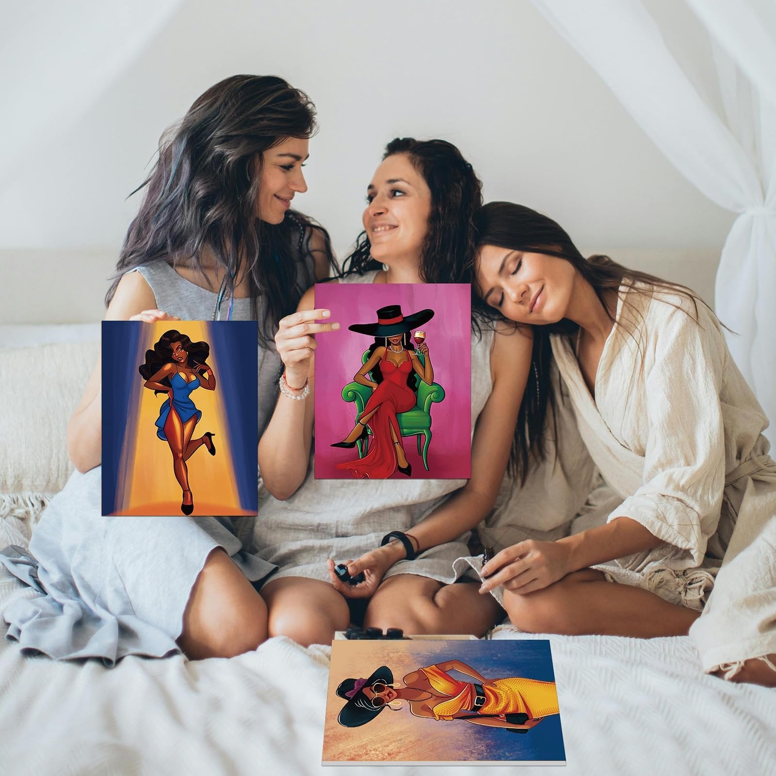 Three women sitting on a bed, holding pre-drawn canvases featuring stylish women. One canvas shows a woman in a blue dress under a spotlight, another a woman in a red dress sitting in a chair, and a third canvas on the bed shows a woman in a yellow dress.