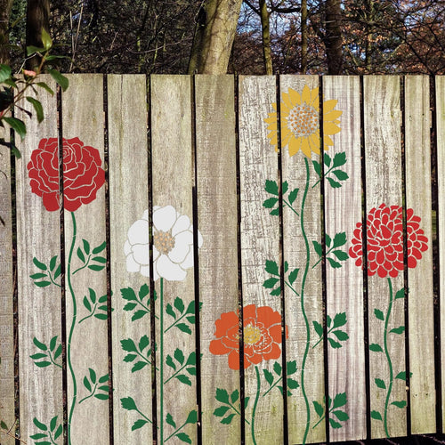 Set of 12 flower stencils applied to a wooden fence, featuring red, white, yellow, and orange floral designs with green stems and leaves.