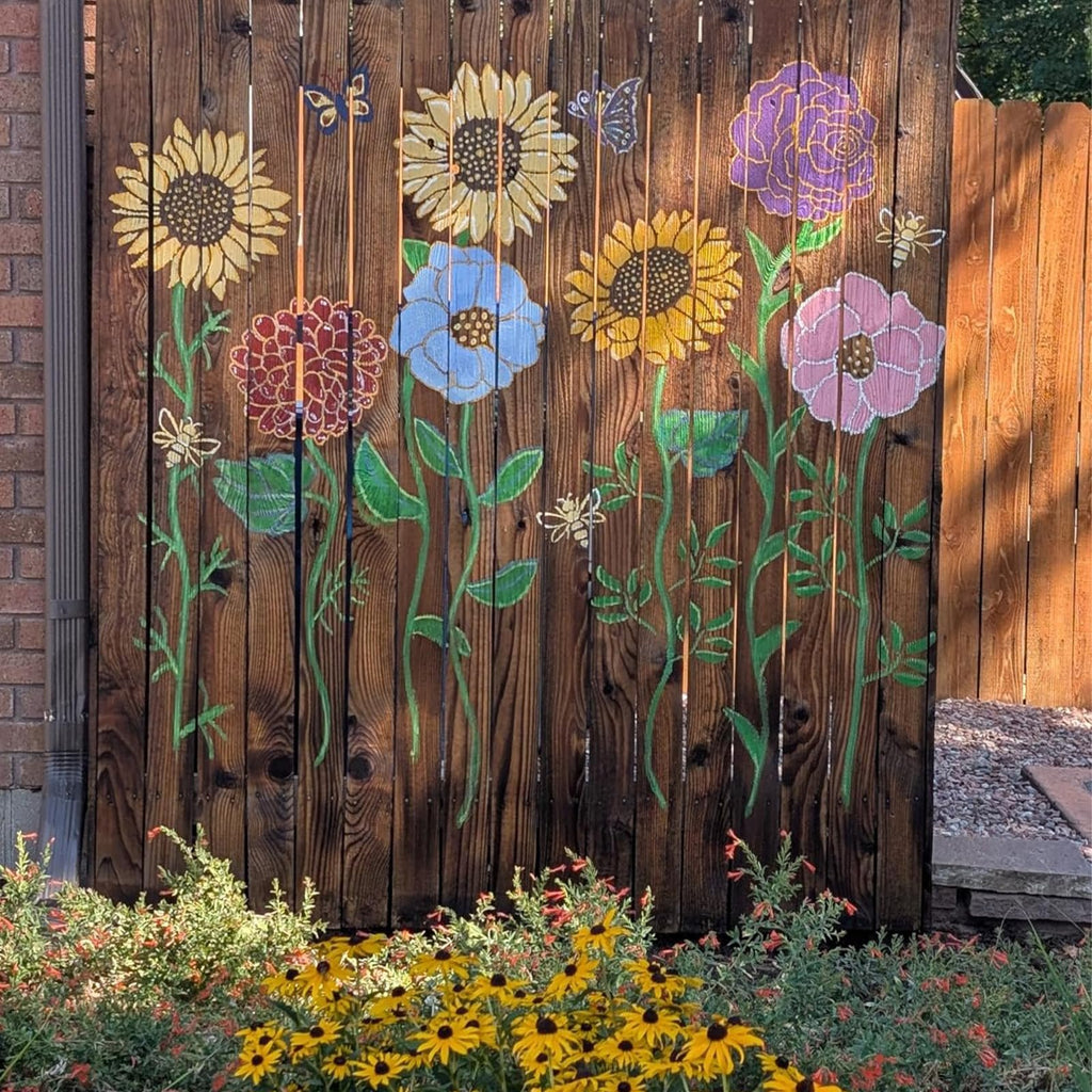 Wooden fence with painted flowers and butterflies, with yellow flowers in the foreground.