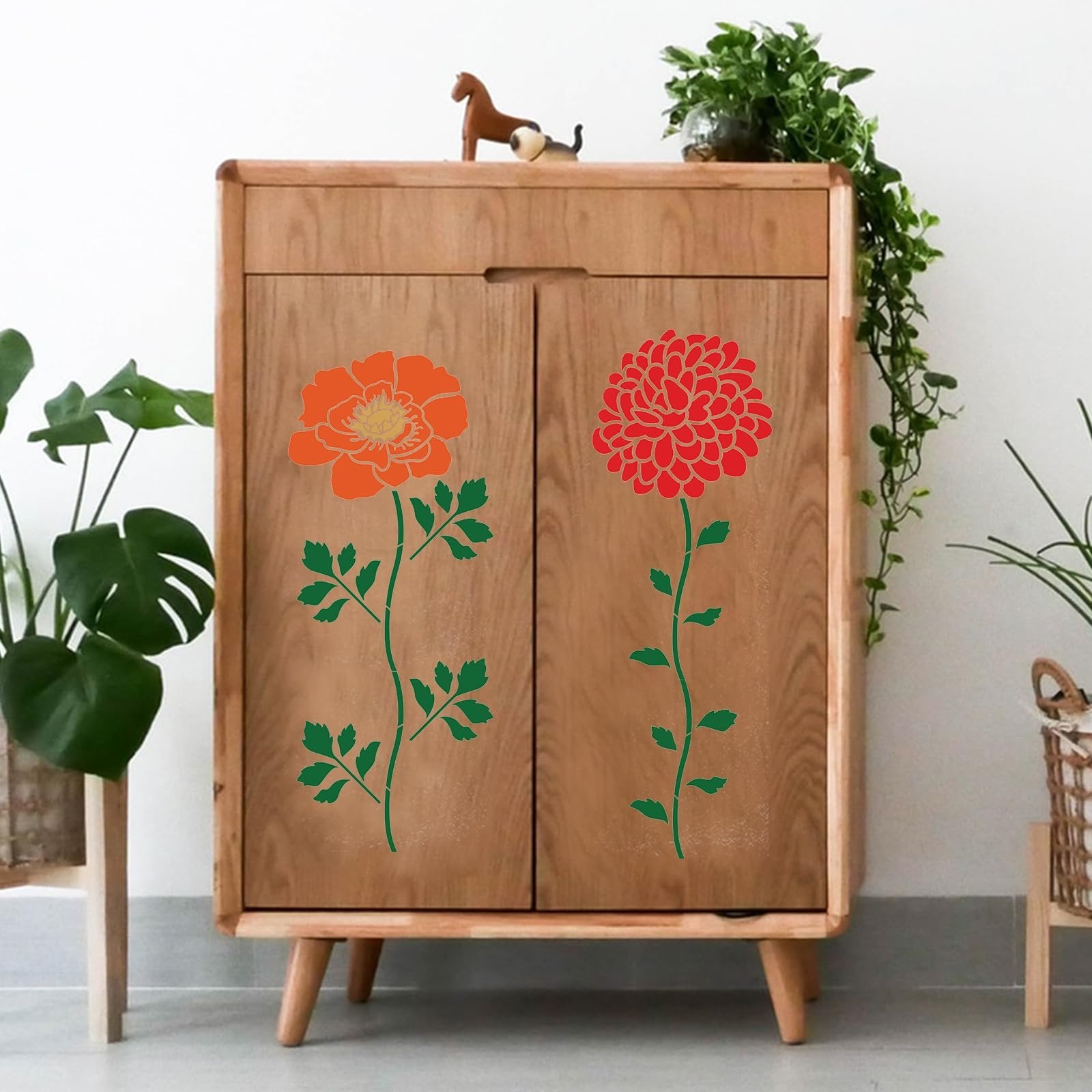 Two floral stencils, one orange and one red, applied to a wooden cabinet door with green stems and leaves.