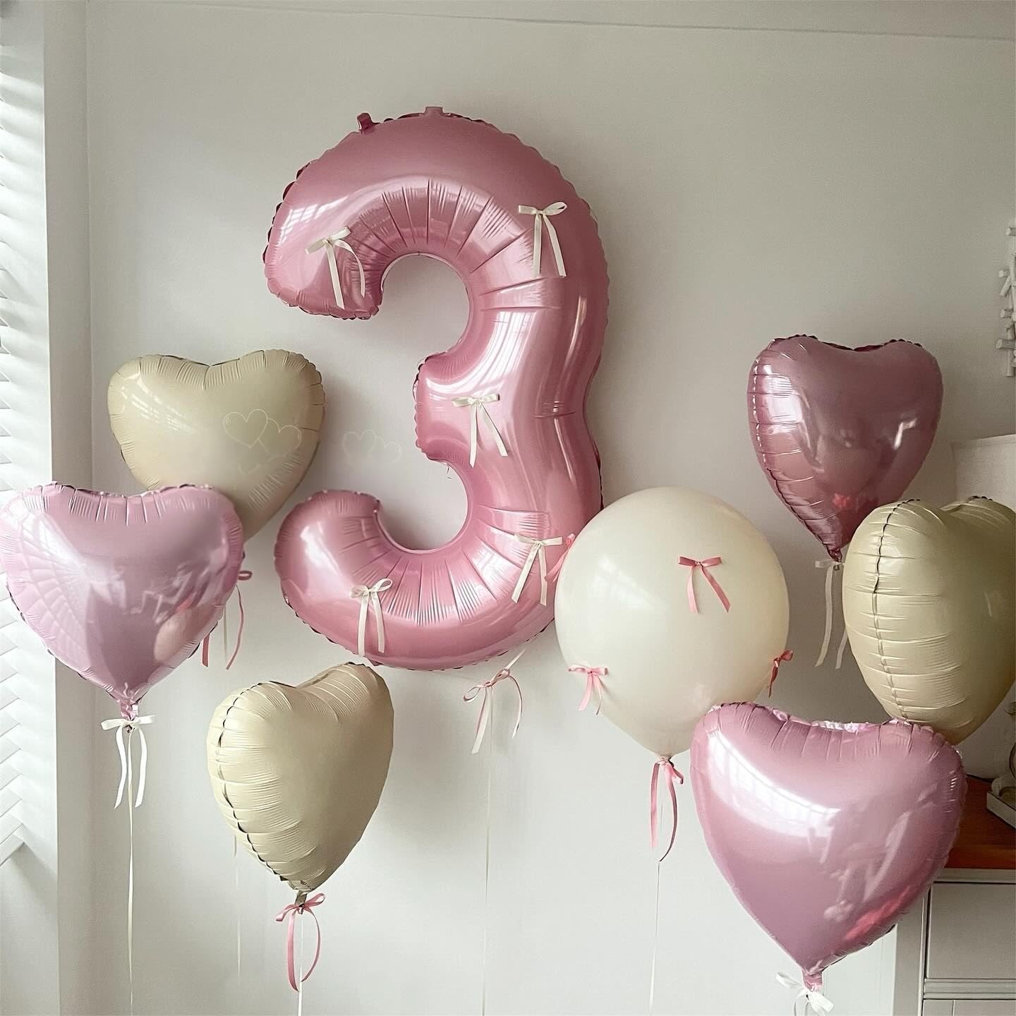 Number 3 balloon and assorted heart balloons in pink, cream, and white, decorated with small bows.