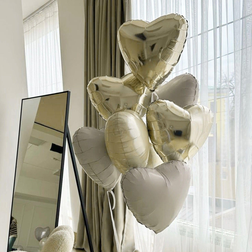 Champagne gold and cream heart-shaped balloons arranged in a bouquet, with a mirror and curtains in the background.