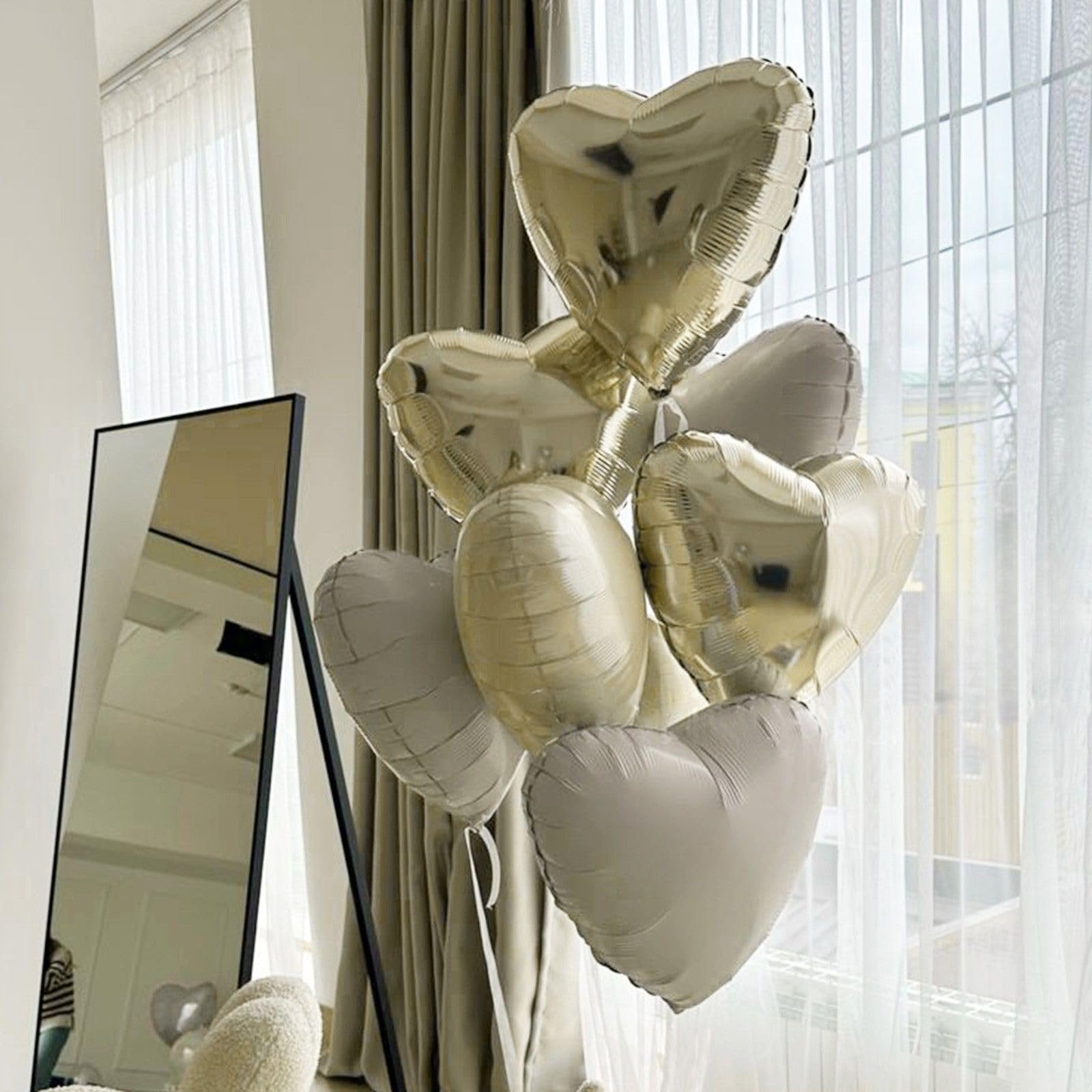 Champagne gold and cream heart-shaped balloons arranged in a bouquet, with a mirror and curtains in the background.