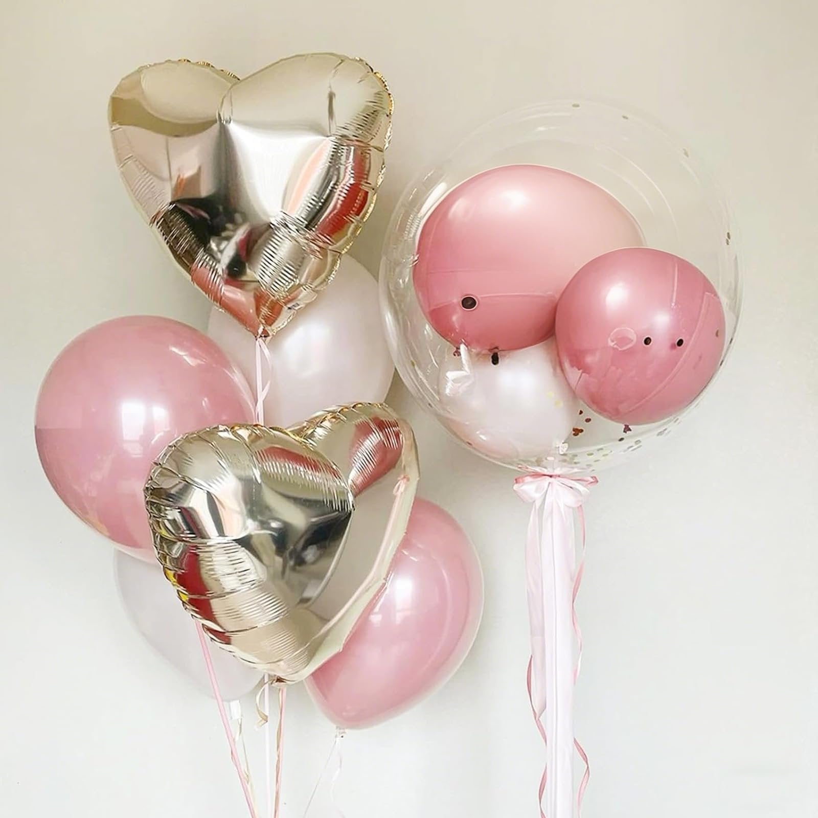 Champagne gold and pink latex balloons, including heart shapes and a clear bubble balloon with smaller balloons inside, tied with pink ribbon.