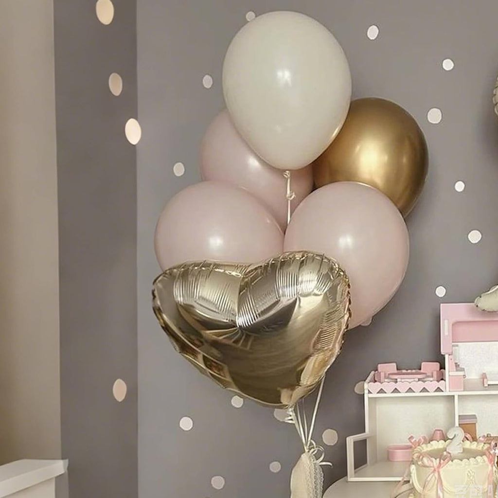 Champagne gold and cream heart and round balloons arranged in a bouquet, with a pink cake and toy kitchen in the background.