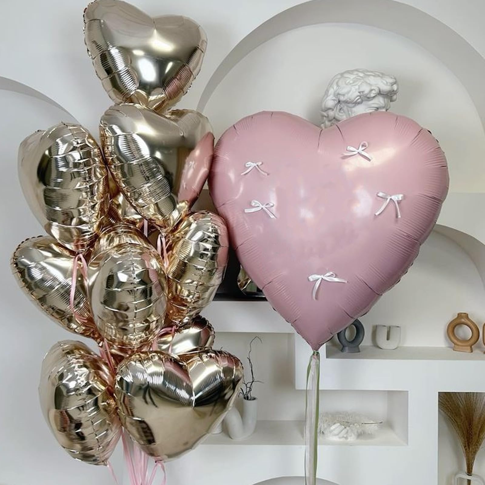 A bouquet of champagne gold and pink heart-shaped balloons with small white bows on the pink balloon, displayed indoors.
