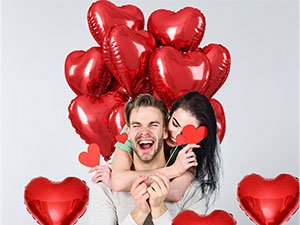 Couple embracing surrounded by red heart-shaped foil balloons, some held by hand
