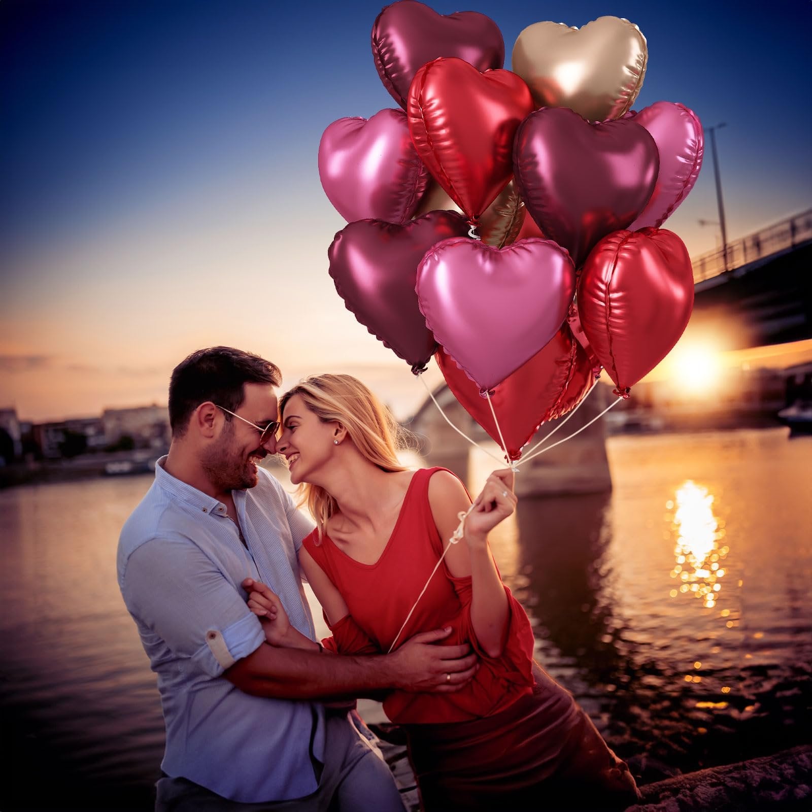 Couple holding a bunch of heart-shaped balloons at sunset by a river