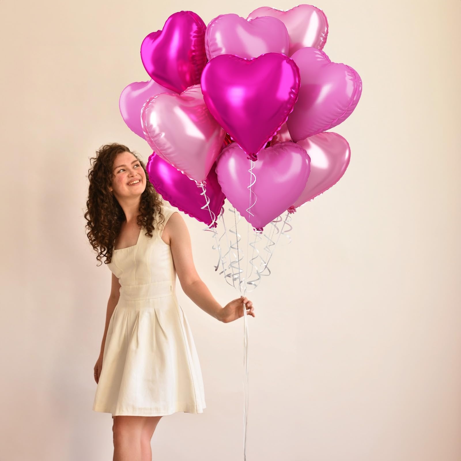 Woman in white dress holding a bouquet of pink and magenta heart-shaped foil balloons