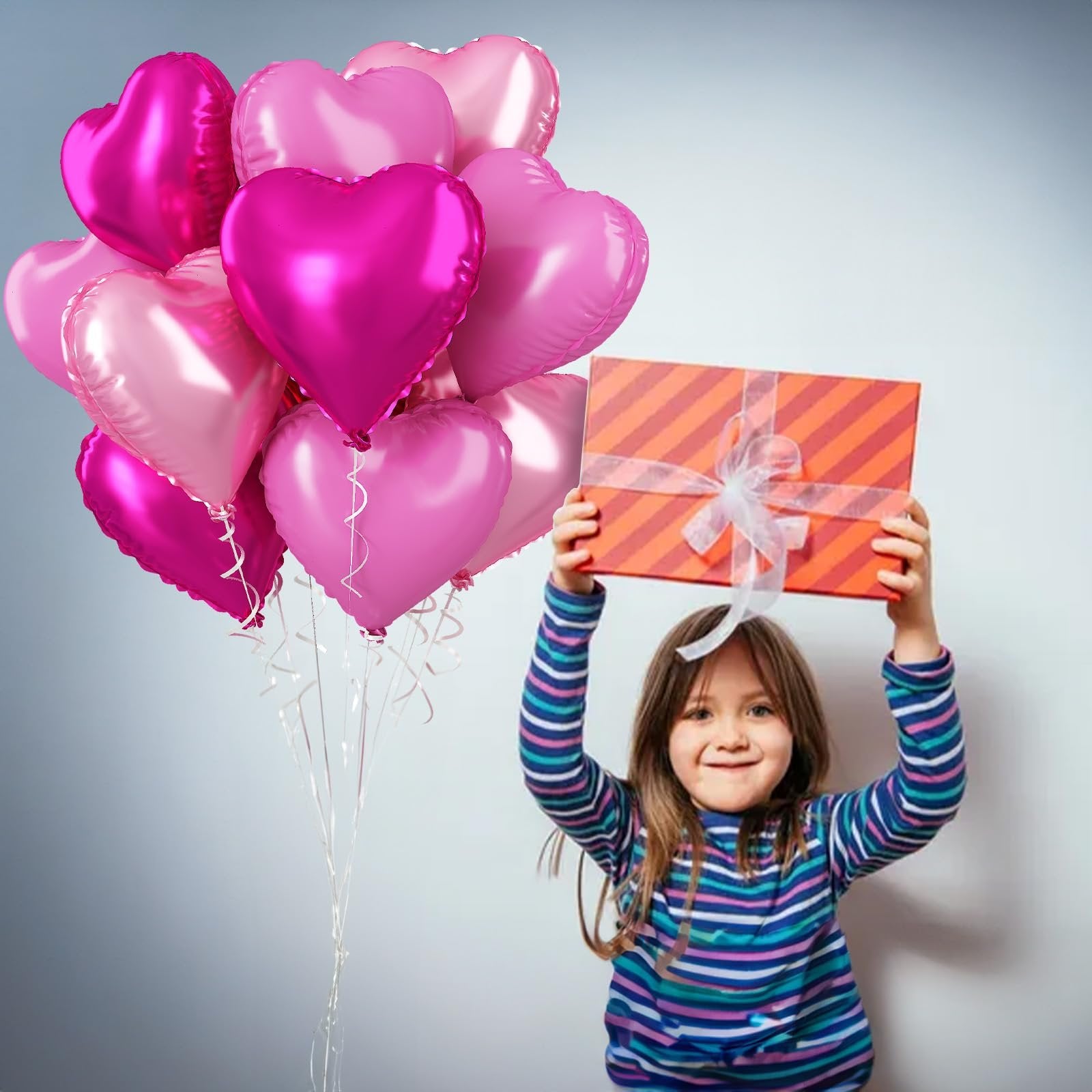 Girl holding a gift box above her head with a bunch of pink heart-shaped balloons