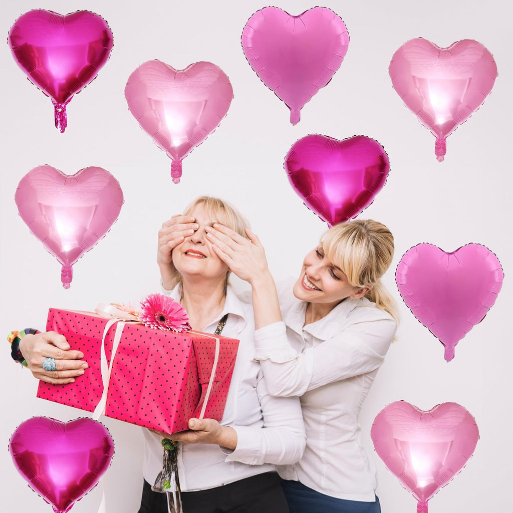 Two women celebrating with pink heart-shaped foil balloons and a gift box.