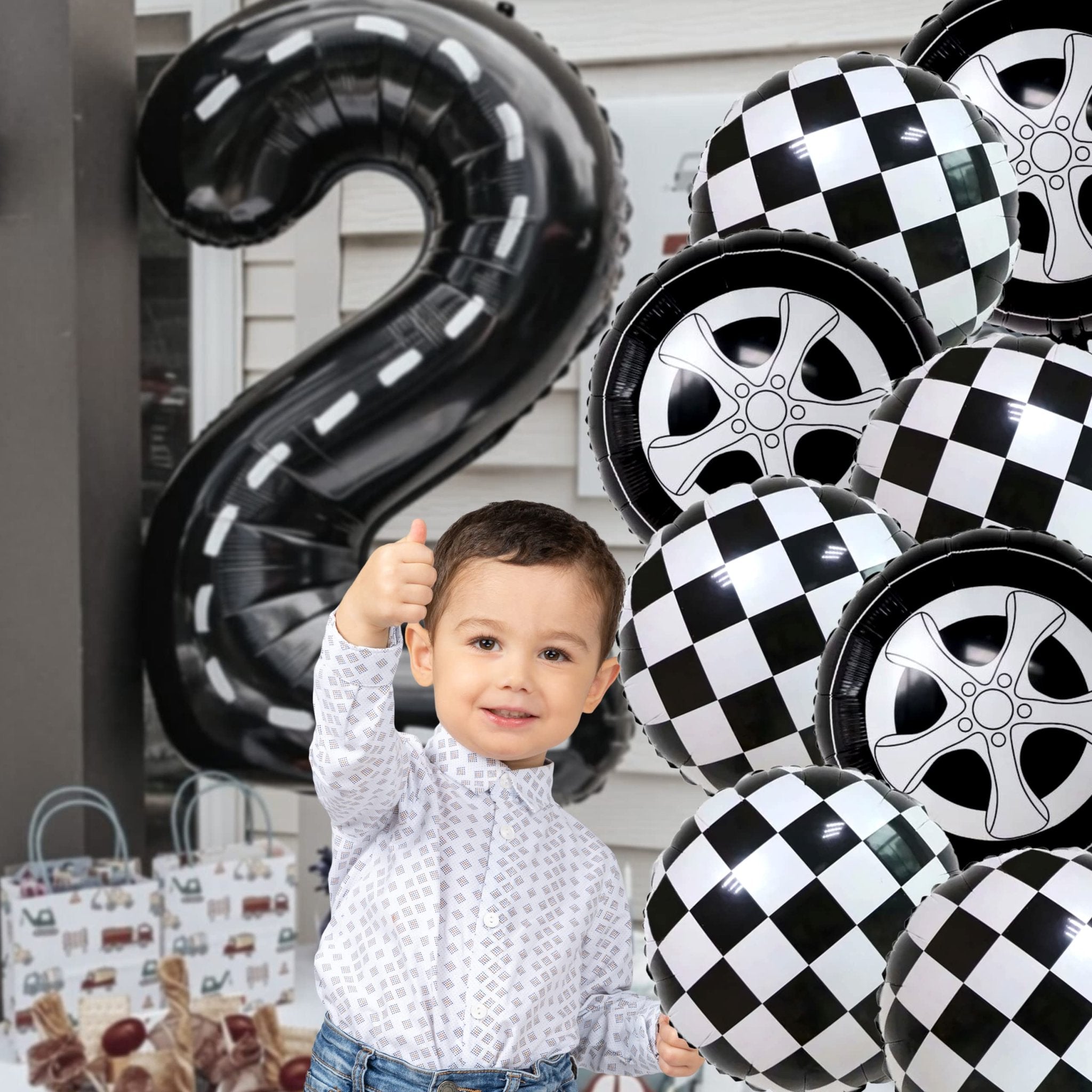 Young boy giving a thumbs up surrounded by race car and checkered balloons