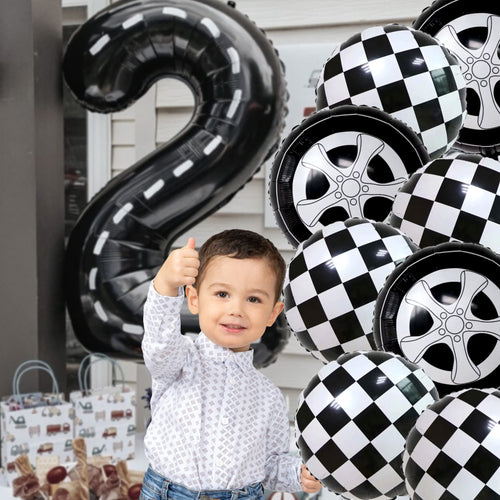 Young boy giving a thumbs up surrounded by race car and checkered balloons