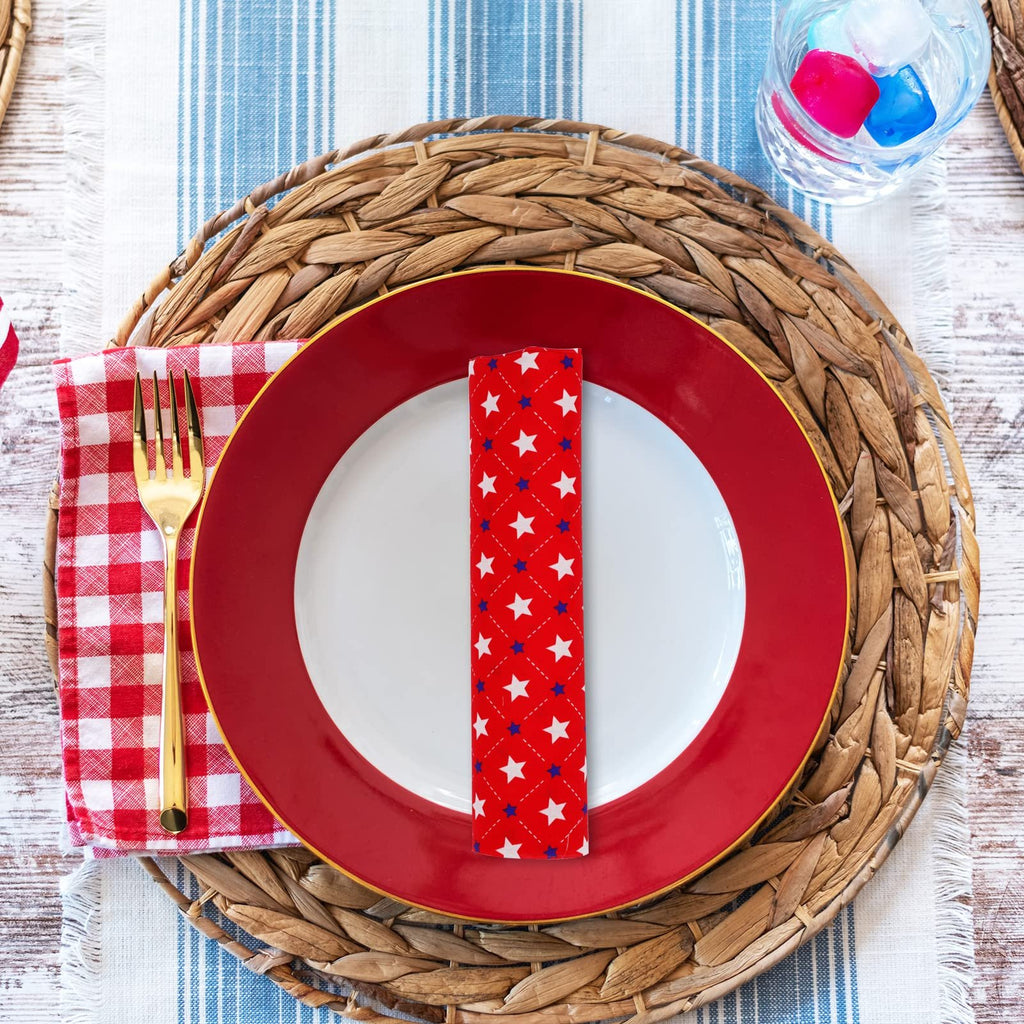 Table setting with red and white checkered napkin, gold fork, red plate, and star-patterned fabric napkin on a woven placemat.
