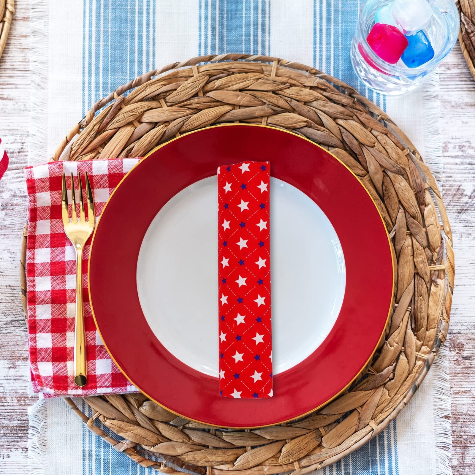 Table setting with red and white checkered napkin, gold fork, red plate, and star-patterned fabric napkin on a woven placemat.