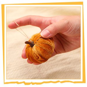 Hand holding a small, fuzzy orange velvet pumpkin ornament with a string for hanging.