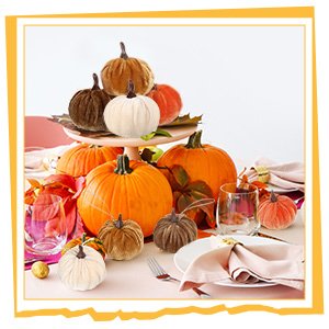 Velvet pumpkins arranged on a table with real pumpkins and fall leaves for decoration.