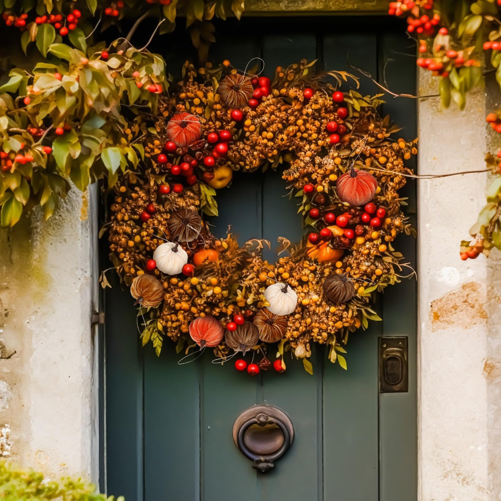 Autumnal wreath with velvet pumpkins and berries hanging on a dark green door.