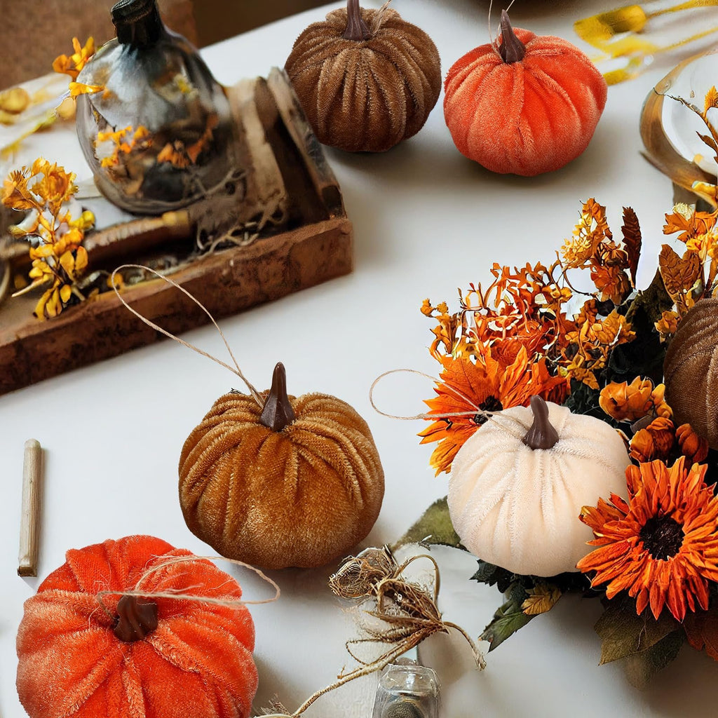 Velvet pumpkins in orange, brown, and cream white arranged with fall foliage and decorative elements on a white surface.