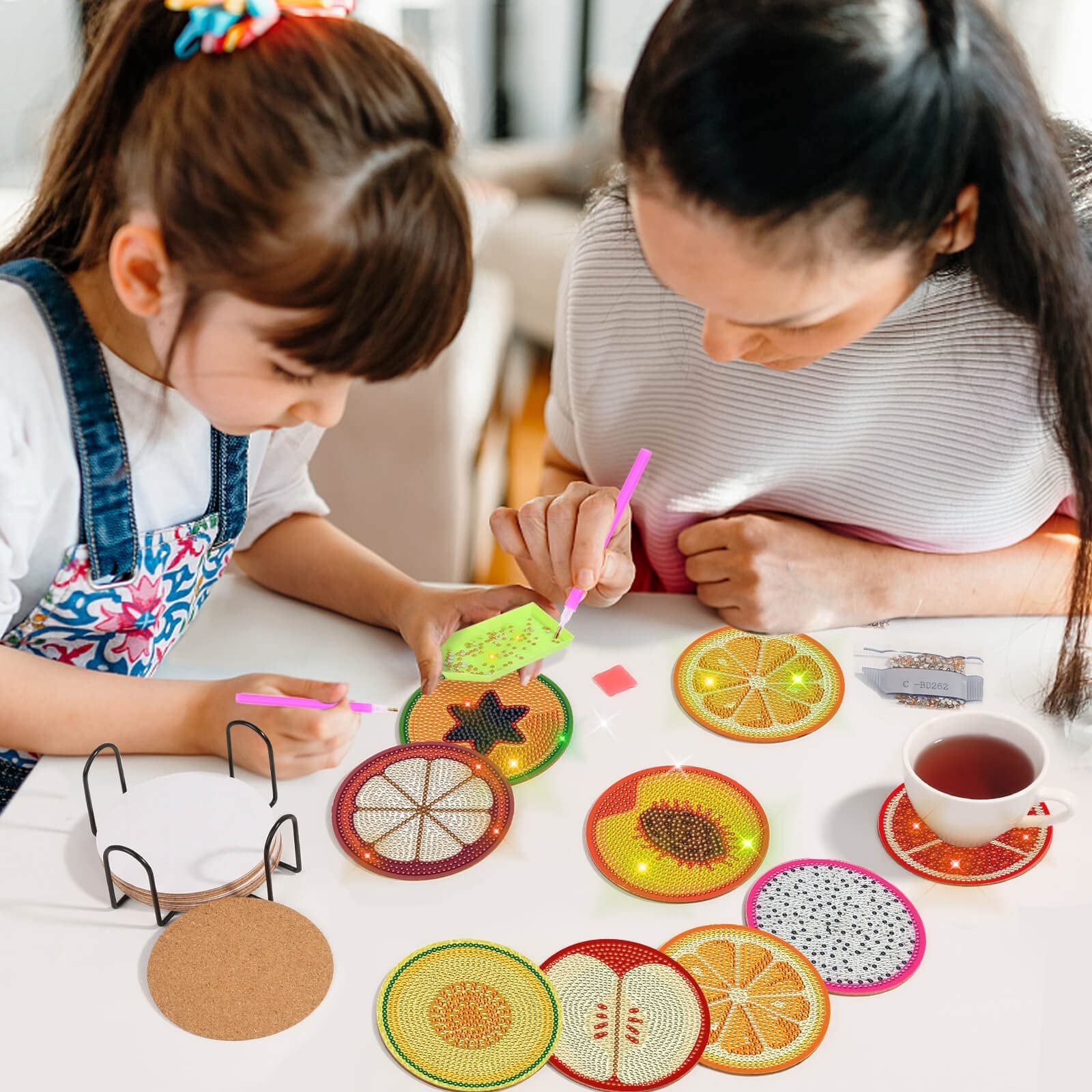 Mother and daughter doing diamond art coasters with fruit designs, kit includes holder and cork bases.