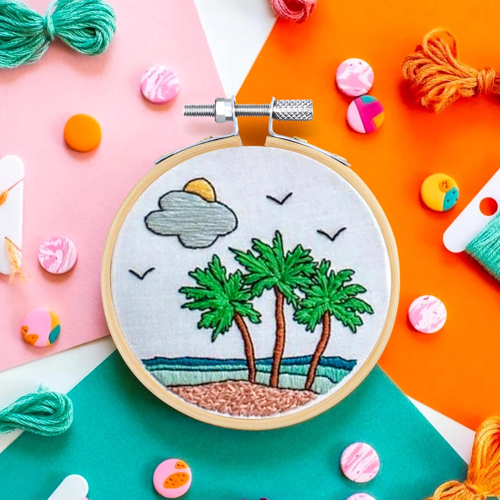 Embroidery hoop with a tropical beach scene, surrounded by colorful threads and craft supplies.
